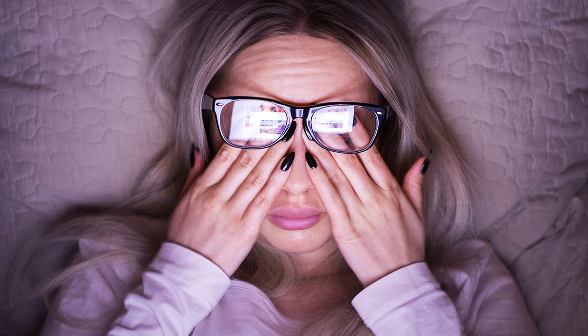 Woman in bed wearing glasses rubbing her eyes