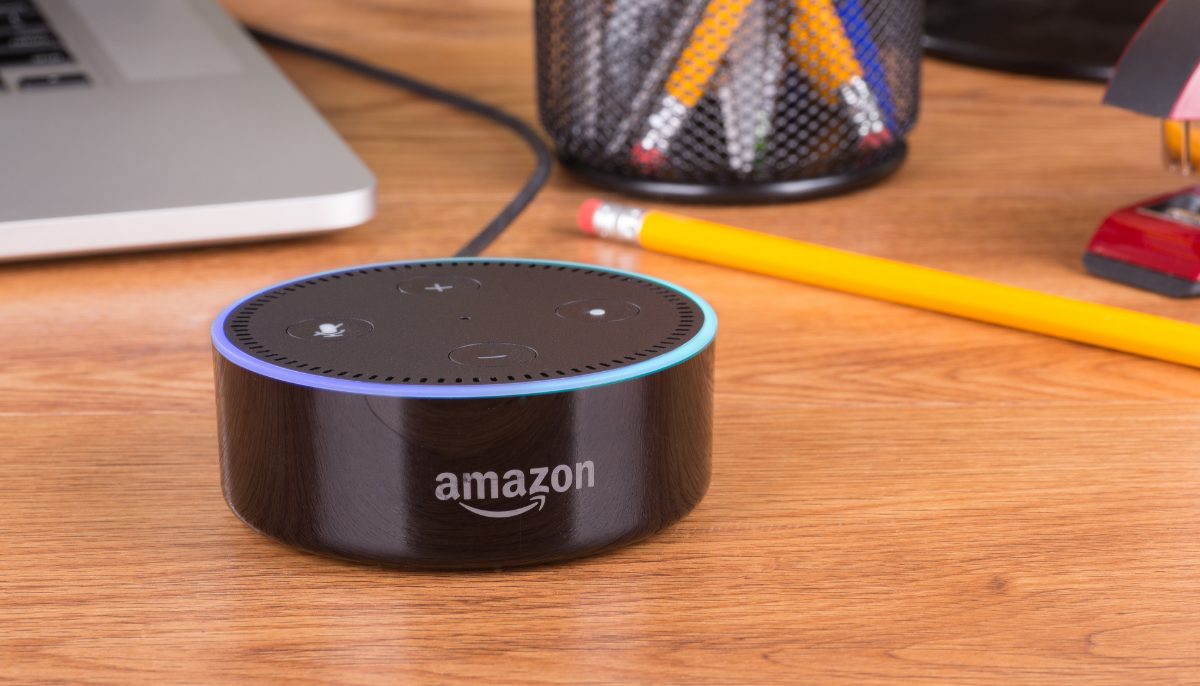 an amazon alexa dot sitting on a desk with pencils and a laptop