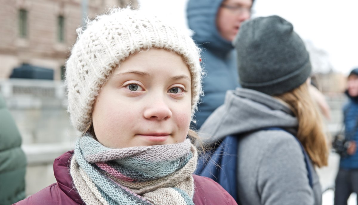 greta thunberg, wearing a hat and scarf, looking at the camera