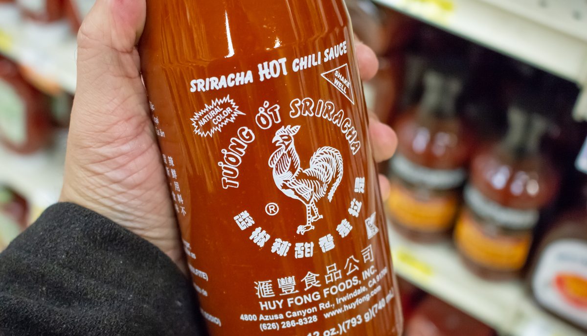 man holding a large bottle of sriracha in a grocery store