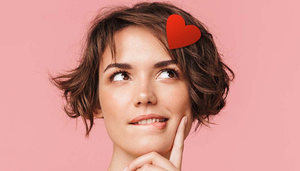 a woman daydreams with a pink background and a heart against her forehead