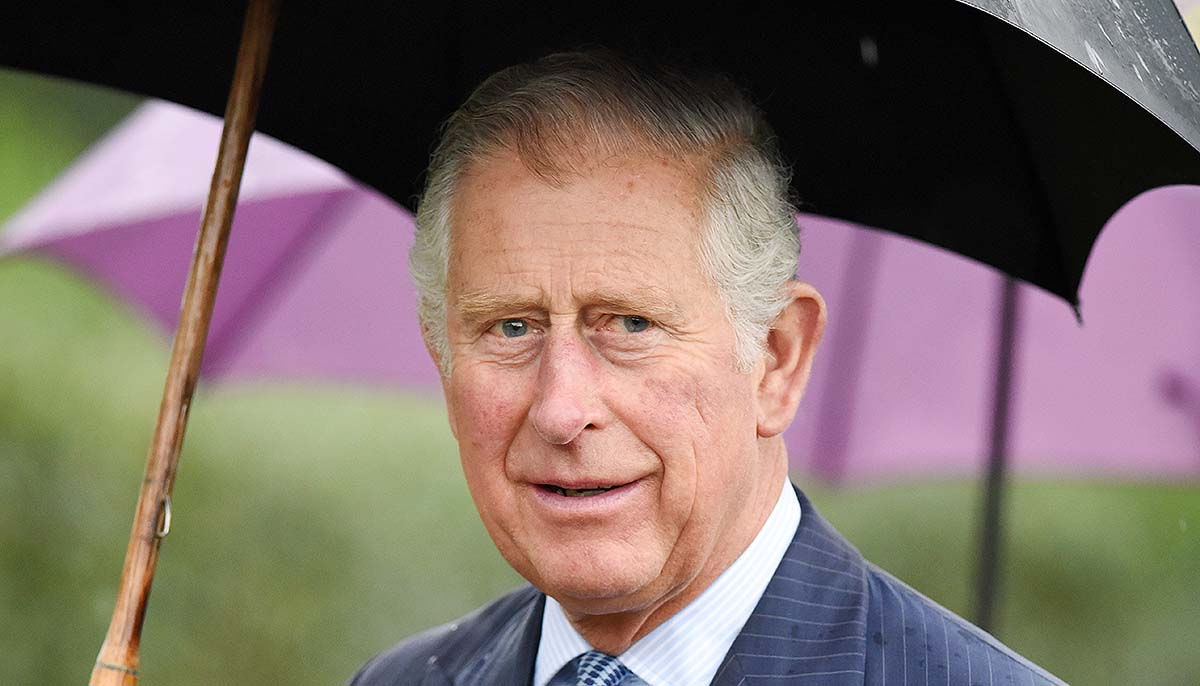 Prince Charles walks outside carrying an umbrella