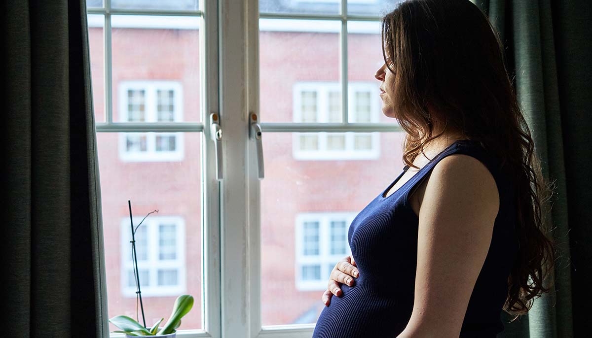 a pregnant woman looks out of a window