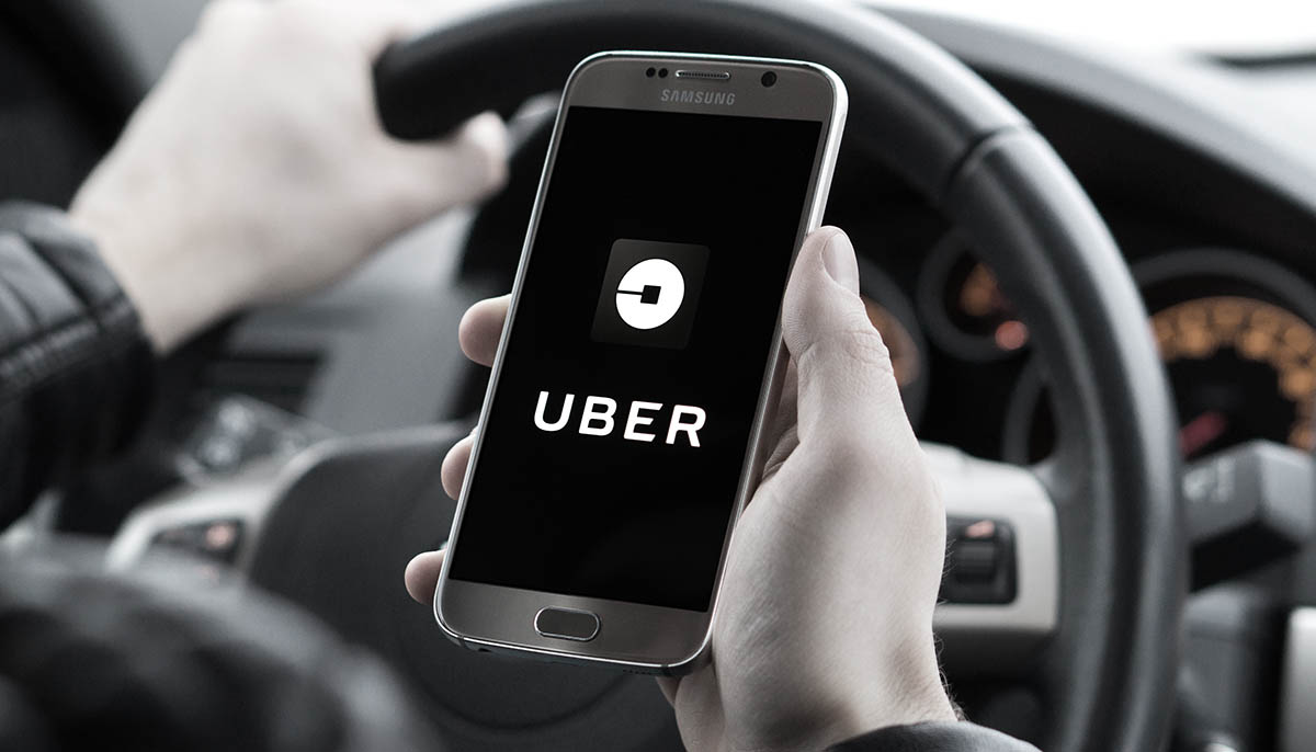 an uber driver holds up a smartphone in his car