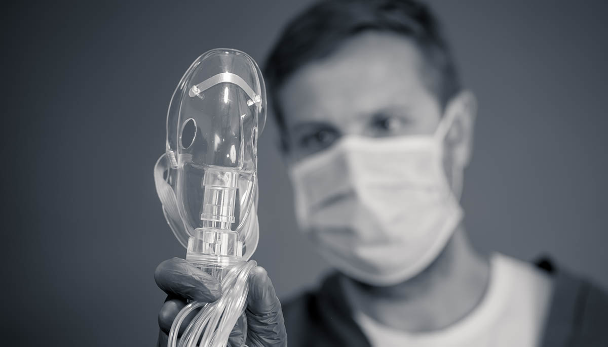 a doctor wearing a face mask holds up a ventilator