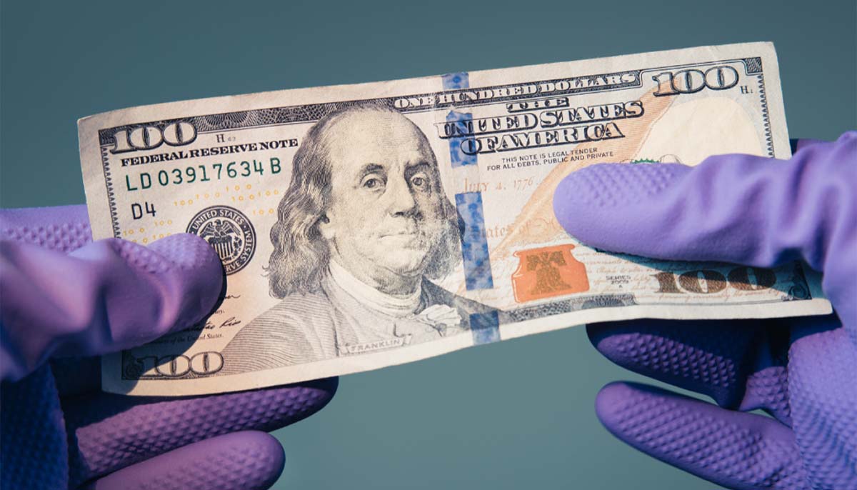 a pair of gloved hands holds a 100 dollar bill