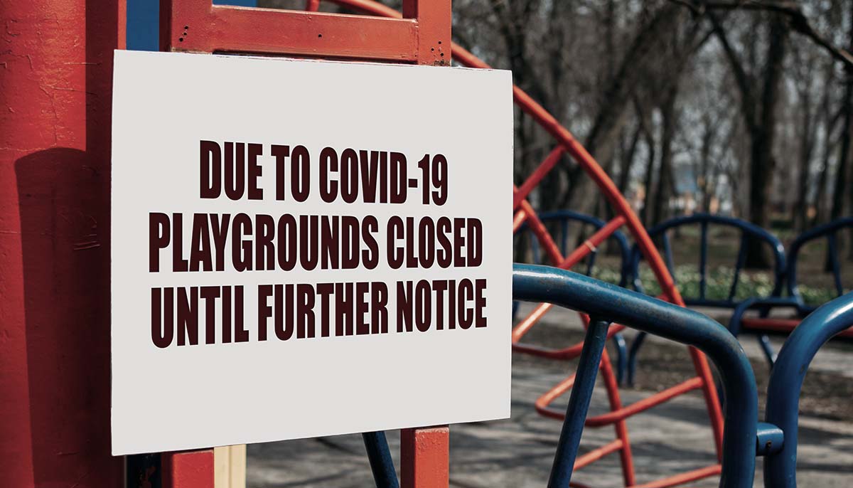  a sign says that the park in the background is closed because of the coronavirus
