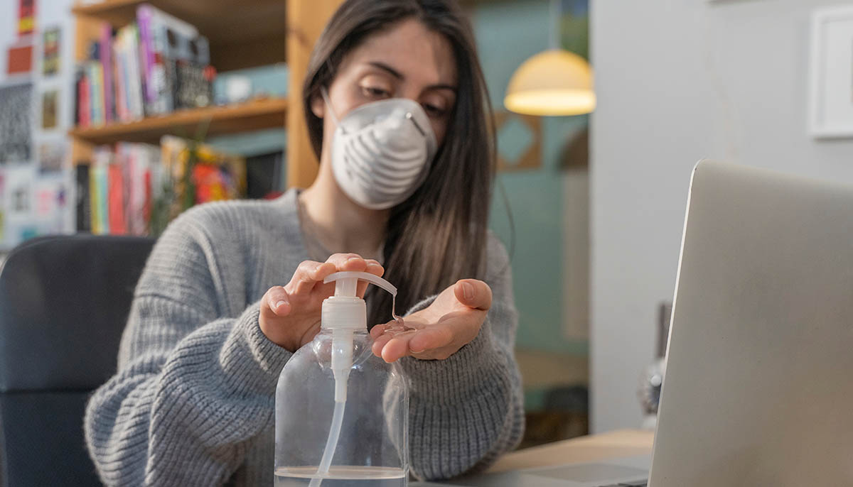 a young woman wearing a face mask cleans her hands with sanitizer