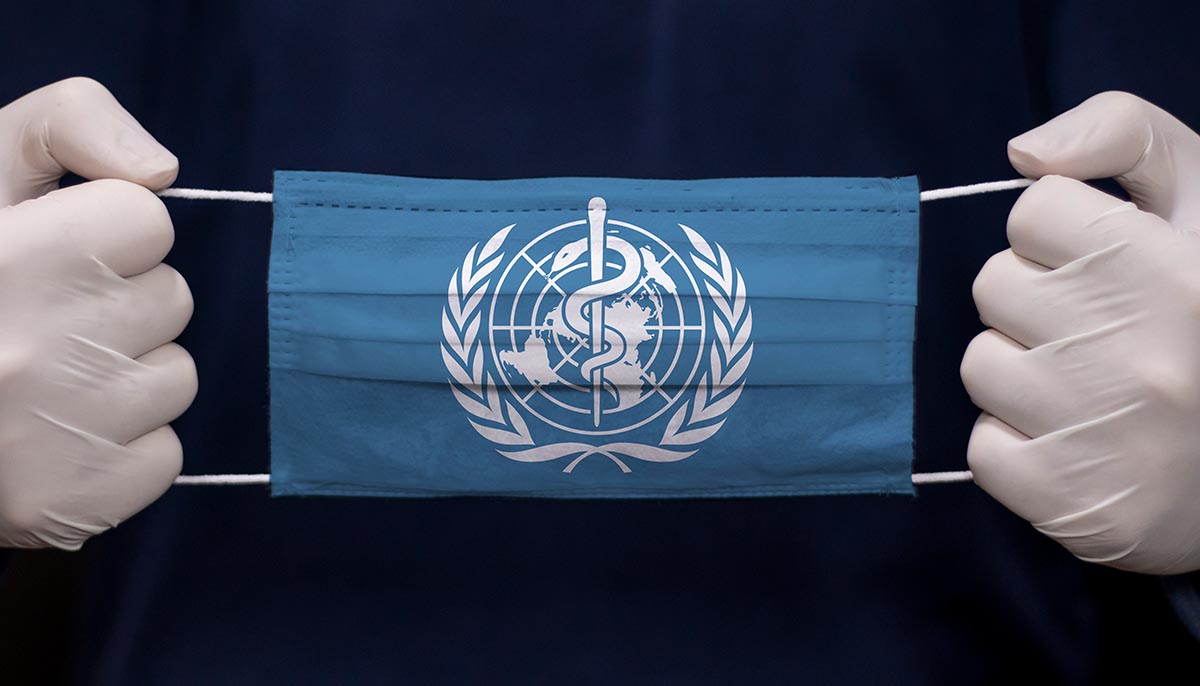 a doctor holds a medical mask with the WHO flag