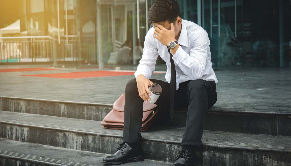 Unemployed man sitting on stairs in front of office building