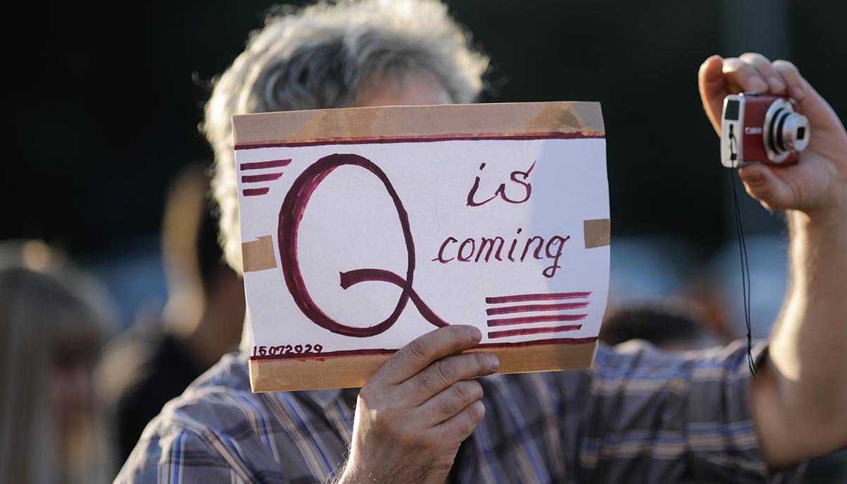 a protester holds up a Qanon message on cardboard