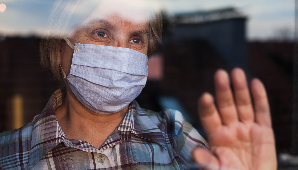 elderly woman looks out of window while wearing face mask