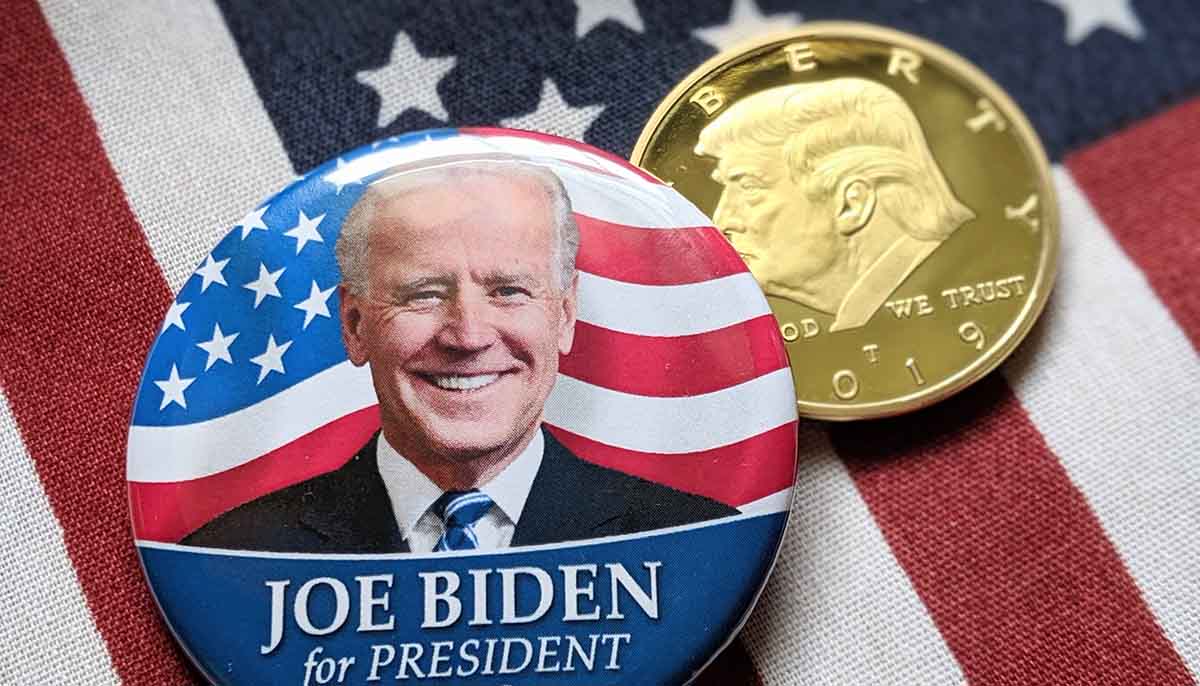 Joe Biden for President button and a Donald Trump gold coin against american flag