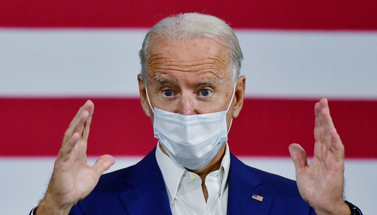 joe biden wearing a mask talking in front of a flag